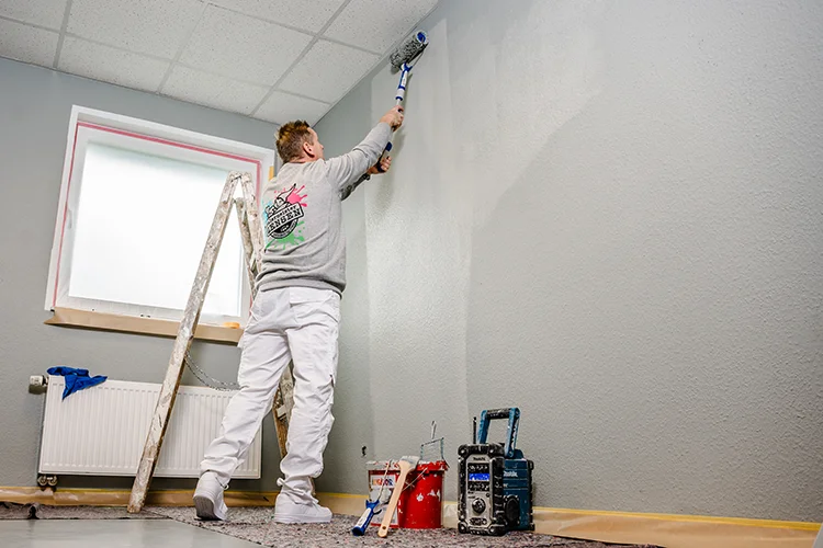 Ein Malergeselle des Malerbetriebs Zensen aus Euskirchen verleiht den Wänden eines Kunden einen frischen Anstrich und ist glücklich bei seiner Arbeit.